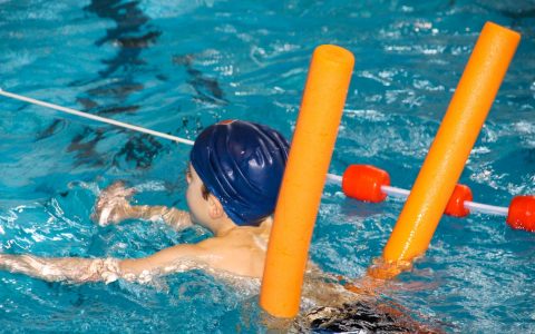 Schwimmkurs, kleiner Junge schwimmt mit Schwimmnudel.